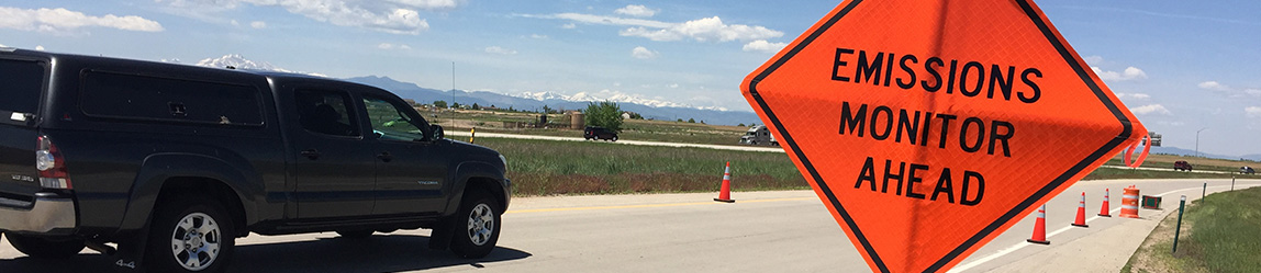 A car driving down the road past a sign telling the driver that image emissions checking is in progress.